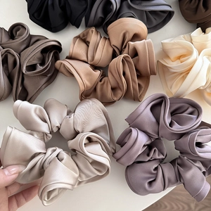 Detailed view of multiple large satin hair scrunchies in various elegant earth tones