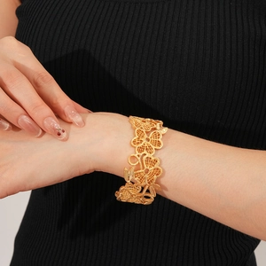 Detail eines goldenen Armreifs mit Blumenmuster, getragen über einem schwarzen Ärmel