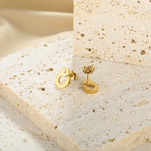 Detailed macro view of gold handcuff-shaped earrings with rhinestones on stone background