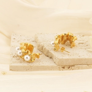 Détail de boucles d'oreilles dorées ondulées avec trois perles sur travertin