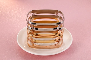 Macro detail of stacked gold, silver and rose gold square bangles on white ceramic dish