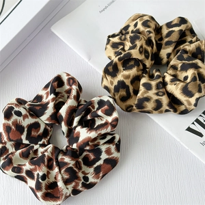 Detail of leopard print satin scrunchies in cream and gold on a minimalist textured background
