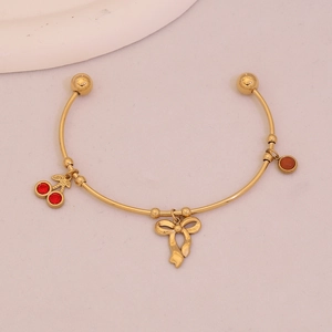 Elegant gold open bangle with red cherry, bow, and brown bead charms on pink background