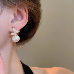 Gros plan de boucles d'oreilles papillon dorées avec perle portées par un mannequin