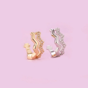 Close-up of wavy gold and silver ear cuffs with sparkling stones on pink backdrop