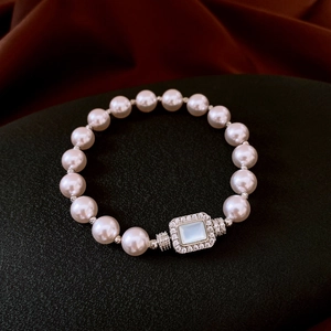 Macro shot of pearl bracelet with diamond-encrusted silver buckle on black textured background