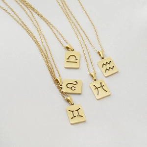 Detailed macro of gold square hollow zodiac pendants on white silk background