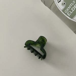 Detail view of a dark green translucent hair claw clip on a minimalist white background