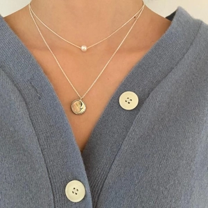 Detail of layered silver necklace featuring a pearl chain and a moon relief coin pendant