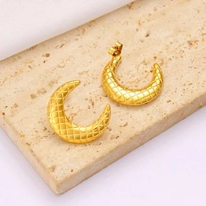 Macro shot of gold crescent earrings with quilted texture on marble and white silk fabric