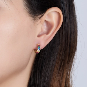 Close-up of golden huggie earrings with rectangle rainbow cubic zirconia on female ear