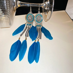 Detail of bohemian sky blue feather earrings with beads and metal disc hanging on glass