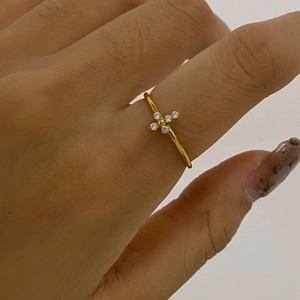 Detail of a thin gold-plated ring featuring a white zircon cross flower on finger
