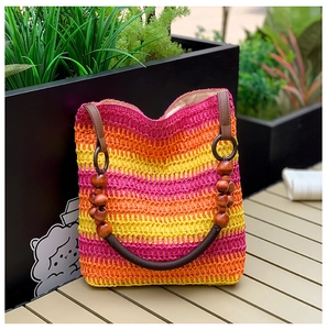 Detail of colorful hand-woven straw beach bag with vibrant rainbow gradient and wood bead handle
