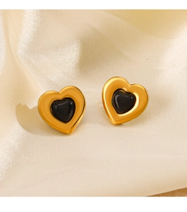 Detail of gold heart earrings with black stone inlay on beige silk fabric backdrop