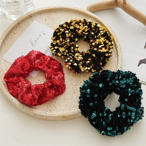 Close-up of sparkling sequin hair scrunchies in red, gold, and black on a decorative tray
