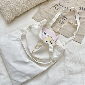 Close-up of minimalist white canvas tote bag with ribbon tie and books inside