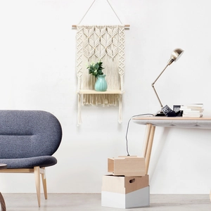 Detail of hand-woven cotton macrame wall hanging shelf with light wood shelf and tassels