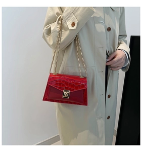 Detail of red crocodile texture flap bag with gold chain strap on beige coat