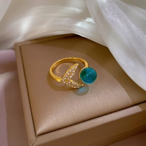 Detail of gold mermaid tail ring with sparkling crystals and a blue pearl bead