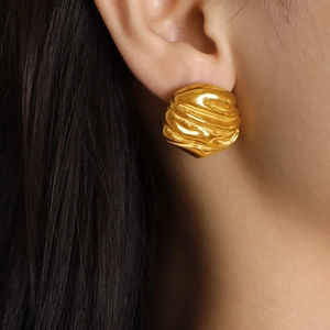 Close-up of irregular textured 18k gold earrings worn on ear with organic liquid ripple design