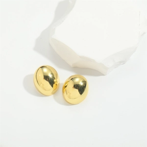Polished gold-plated oval stud earrings displayed on a white decorative stone base