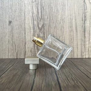 Detail view of square glass perfume spray bottle with gold nozzle and cap on wood surface