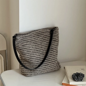 Détail du sac fourre-tout en tricot à rayures grises avec anses en cuir noir sur fond blanc