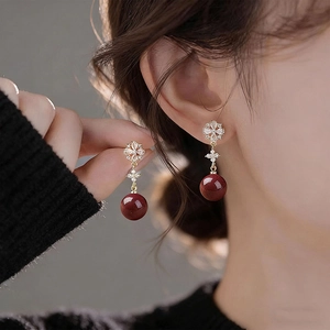 Close-up of elegant red bead earrings with gold flower studs worn by a model