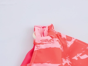 Detail of pink floral dress featuring a white circular buckle on the shoulder strap