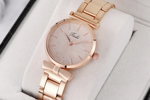 Detail of rose gold ladies watch with bow decor and leaf pattern dial on white cushion