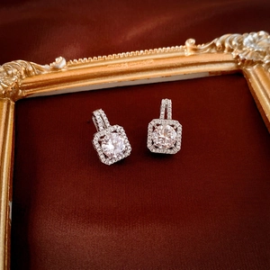 Macro shot of silver square halo earrings with sparkling zircon on a red velvet background
