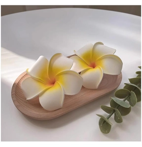 Close-up of two realistic EVA foam Frangipani flowers in a wooden tray with green leaves