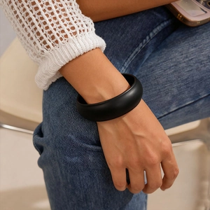 Close-up of a matte black acrylic chunky bangle bracelet on a model's wrist with casual outfit
