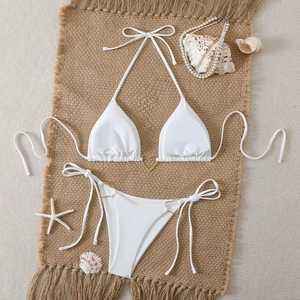 Flat lay of white triangle bikini set with gold heart rings on a beach-themed background