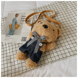 Detail of plush brown teddy bear crossbody bag wearing blue denim overalls and a bow