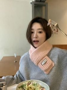 Close-up of pink knitted scarf with KN STUDIO label worn by woman in cafe