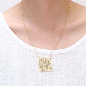 Detail of a square cutout city map pendant necklace in gold worn by a model