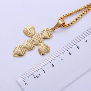 Detail view of gold heart cross pendant with textured finish next to a measuring ruler