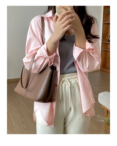 Close-up of a brown PU leather tote bag styled with a pink shirt and white trousers