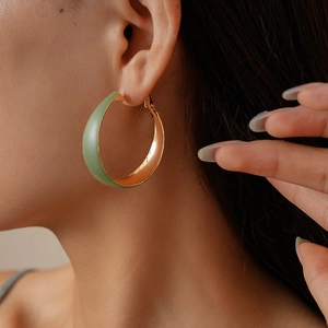 Close-up of sage green enamel and gold-toned C-shaped hoop earrings on female model
