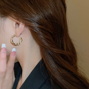 Detail view of gold C-shaped hoop earring with lava texture and tiny diamonds on a model
