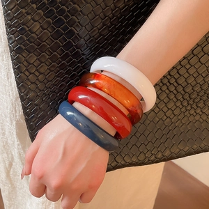 Detail view of multi-color resin bangles in amber, red, blue and white on a model's wrist