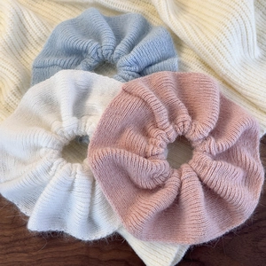 Detailed texture of knit ruffle scrunchies in blue, white, and pink on a soft sweater