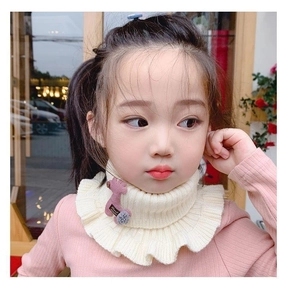 Detail of a beige knitted kids neck warmer with ruffled edges and handmade label