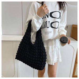 Detail of black cloud puff handbag with pleated texture carried by model in minimal setting