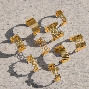 Close-up of assorted gold 18k plated stainless steel rings on a grey stone background