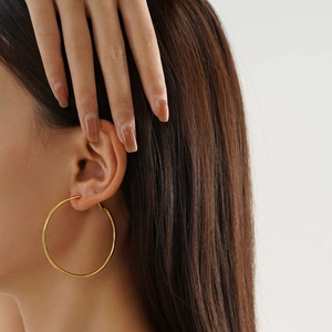 Close-up of a large gold polished stainless steel hoop earring worn by a model