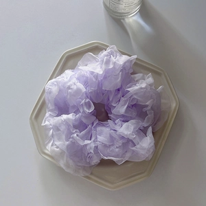 Close-up of a purple ruffled chiffon hair scrunchie placed on a white porcelain plate