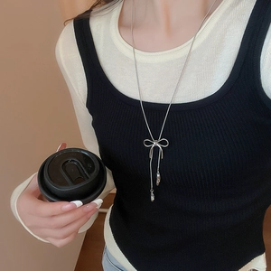 Silver bow pendant necklace with tassel chains worn over a black and beige outfit